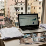 Mesa com notebook e planilha de controle de imóveis encalhados no mercado imobiliário brasileiro